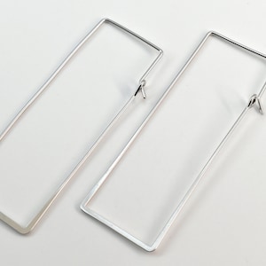 May include: A pair of silver rectangular hoop earrings. The earrings are simple and modern in design.