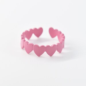 May include: A pink adjustable ring with a series of connected heart-shaped charms.