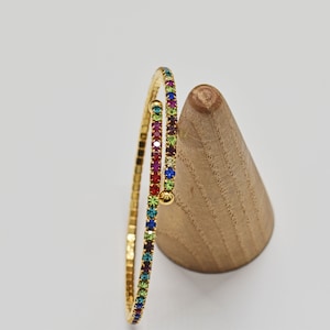May include: A gold bangle bracelet with a rainbow of colorful rhinestones.