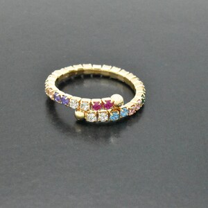 May include: A gold ring with a colorful, multi-gemstone design. The ring is made of a flexible material and features a variety of colors, including blue, green, pink, and red.