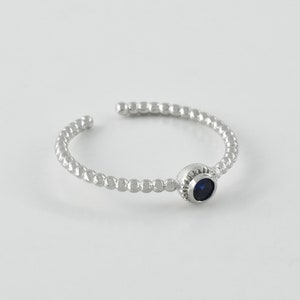 May include: A silver ring with a beaded band and a small blue gemstone.
