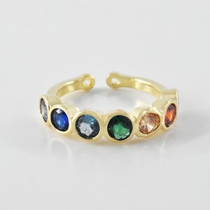 May include: Gold ring with a row of colorful gemstones. The stones are blue, light blue, green, orange, and red.