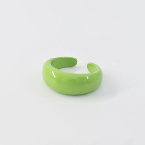 Puede incluir: Un anillo de plástico brillante de color verde brillante, con forma redondeada.