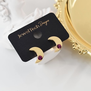 May include: A pair of gold crescent moon earrings with a small purple rhinestone in the centre of each moon.