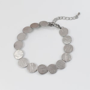 May include: A silver bracelet with a chain closure and a series of round, textured metal discs.