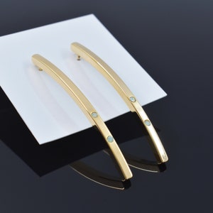 Puede incluir: Un par de pendientes de oro con tres pequeñas piedras de color azul claro en cada pendiente.