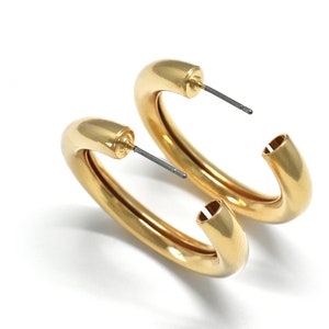 May include: A pair of gold hoop earrings with a thick, rounded design. The earrings are made of metal and have a simple, elegant style.