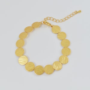 May include: A gold bracelet with a chain and a series of round, textured, gold discs.