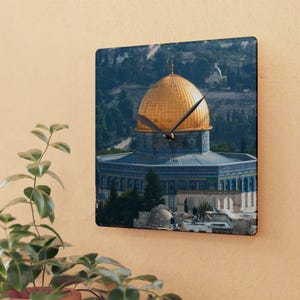 May include: A clock with a gold dome and blue and white tiled exterior. The clock is set against a backdrop of a cityscape with trees and buildings.