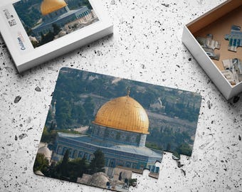 May include: A completed jigsaw puzzle of the Dome of the Rock in Jerusalem. The puzzle shows the golden dome and blue and white tiled exterior of the mosque. The puzzle is set against a backdrop of a cityscape.