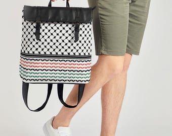 May include: A backpack with a black leather top flap and handle, featuring a white and black geometric pattern on the main body. The bottom section has horizontal stripes in red, green, and black. The bag has black straps and buckles.