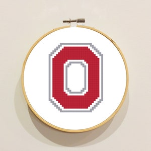 May include: A red and gray embroidered letter O in a circular embroidery hoop.