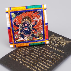 Op de afbeelding: Een vierkante geborduurde patch met een gedetailleerde illustratie van een godheid met meerdere armen en een felle uitdrukking, omringd door vlammen. De patch is omlijst met kleurrijke draden en ligt op een donkere kaart met gouden tekst "Mahakala".