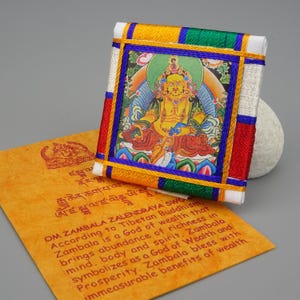Peut inclure: Un petit drapeau de prière carré en tissu blanc avec une bordure colorée. Le drapeau représente une peinture d'une divinité dorée assise sur un trône de lotus. Le texte sur le drapeau est "OM ZAMBALA ZALENDRAYA SWO". Selon le bouddhisme tibétain, Zambala est un dieu de la richesse qui apporte l'abondance de la richesse dans l'esprit, le corps et l'esprit. Zambala symbolise un dieu de la richesse et de la prospérité. Zambala bénit avec des avantages incommensurables de la richesse.