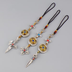 Pode incluir: Três pingentes ornamentados em prata e ouro com cordões pretos. Cada pingente apresenta um design circular central com um centro dourado e detalhes azuis, conectado por elementos decorativos e terminando em um pingente em forma de adaga ou cruz.