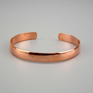 Puede incluir: Un brazalete simple de cobre. El brazalete es liso y brillante, con una forma ligeramente redondeada.
