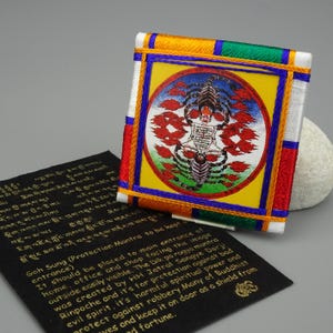 Peut inclure: Un carré brodé coloré avec un fond jaune et une image circulaire d'un scorpion au centre. Le scorpion est entouré de flammes et l'image est entourée d'une bordure bleue. Le carré est bordé de tissu rouge, vert, jaune et bleu.