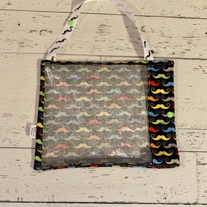May include: A black fabric bag with a clear plastic window. The bag has a white strap and a colorful mustache pattern. The bag is perfect for storing small items.
