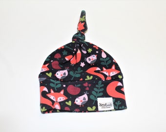 May include: A black, red, and green baby hat with a fox and bird pattern. The hat has a knot on top and a small white label that says "Made with Love, Sew Much More".