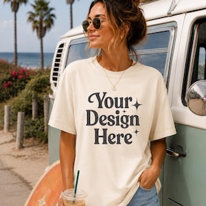 May include: A cream-colored short-sleeve t-shirt featuring the black text "Your Design Here" printed on the front, accented by small four-pointed star symbols. The shirt has a crew neckline and a relaxed fit, made of a solid cotton-like fabric.