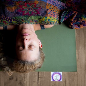 May include: A woman lies on a green yoga mat with her eyes closed. She is wearing a colorful patterned shawl. The mat is on a wooden floor. A small card with the text "NOT TODAY" is visible in the lower right corner of the image.