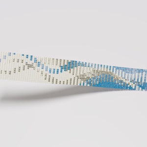 May include: Close-up of a beaded bracelet with a geometric pattern. The bracelet features a combination of white, silver, and blue beads. The beads are intricately woven together to create a textured surface. The word ".blue" is in the bottom right corner.