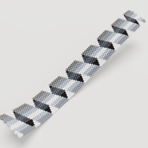 May include: A beaded bracelet featuring a geometric pattern in shades of gray, white, and black. The bracelet is made of small, evenly spaced beads, creating a textured surface. The design has a repeating chevron-like pattern.