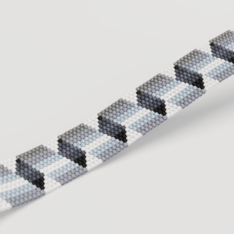 May include: Close-up of a beaded bracelet with a geometric pattern. The bracelet features a repeating design of gray, black, and white beads. The beads are arranged in a chevron pattern, creating a textured look. The bracelet is displayed against a white background.