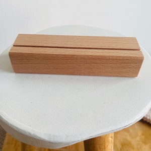 K&ouml;nnte beinhalten: Ein nat&uuml;rlicher Holzst&auml;nder mit zwei Schlitzen zum Halten von Karten oder Schildern. Der St&auml;nder ist aus hellbraunem Holz gefertigt und steht auf einer wei&szlig;en Oberfl&auml;che.