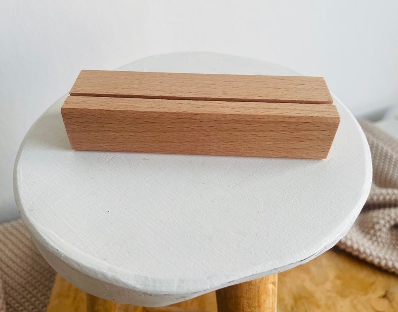 K&ouml;nnte beinhalten: Ein nat&uuml;rlicher Holzst&auml;nder mit zwei Schlitzen zum Halten von Karten oder Schildern. Der St&auml;nder ist aus hellbraunem Holz gefertigt und steht auf einer wei&szlig;en Oberfl&auml;che.