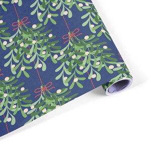 Pu&ograve; includere: Rotolo di carta da regalo con un motivo ripetuto di foglie verdi di vischio, bacche bianche e fiocchi rossi su sfondo blu scuro. La carta &egrave; arrotolata, mostrando il motivo.