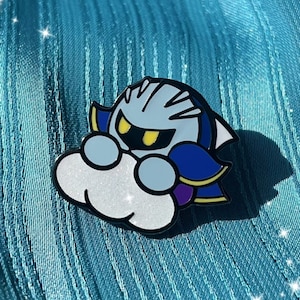 Może przedstawiać: Emaliowana przypinka w kolorze srebrnym i niebieskim przedstawiająca kreskówkową wersję postaci z gry wideo Meta Knight z serii Kirby. Meta Knight jest przedstawiony ze swoim charakterystycznym mieczem i hełmem i unosi się na białej chmurze.