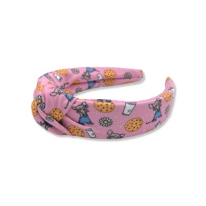 May include: Pink knotted headband with a repeating pattern of a cartoon mouse holding a glass of milk and a cookie.