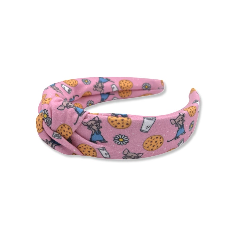 May include: Pink knotted headband with a repeating pattern of a cartoon mouse holding a glass of milk and a cookie.