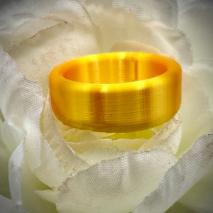 May include: A gold-colored ring with a smooth, brushed finish. The ring is thick and has a rounded shape.