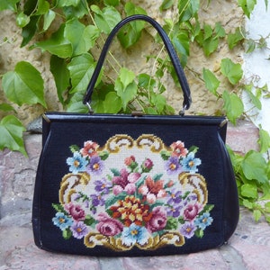 Könnte beinhalten: Eine schwarze Ledertasche mit einem floralen Stickmuster. Die Stickerei zeigt einen Strauß aus rosa, lila, gelben und blauen Blumen auf cremefarbenem Hintergrund.
