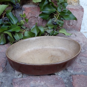 Può includere: Una pirofila ovale in ceramica marrone con interno marrone chiaro. La pirofila è appoggiata su una superficie di mattoni.