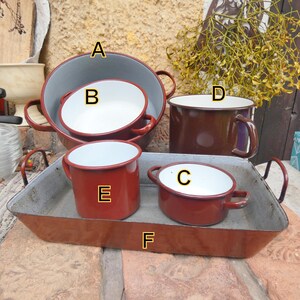 Puede incluir: Colección de artículos de cocina de esmalte vintage. Incluye un cuenco grande gris y rojo, un cuenco más pequeño blanco y rojo, una taza marrón, dos tazas rojas y una bandeja rectangular. Los artículos tienen bordes y asas rojas.