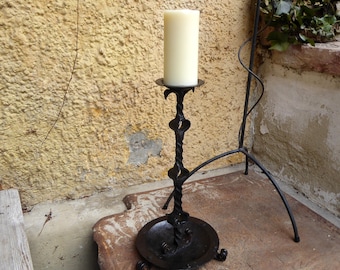 May include: A black metal candle holder with a twisted design and a white candle. The candle holder is sitting on a brown surface.