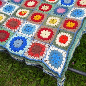 Könnte beinhalten: Eine bunte Häkeldecke mit verschiedenen Quadraten in unterschiedlichen Farben und Mustern, darunter Rot, Blau, Grün, Gelb und Braun.