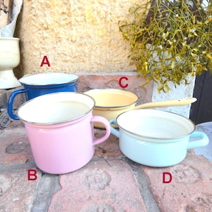 Può includere: Quattro pentole e tazze in smalto di vari colori: blu, rosa, giallo e azzurro. Ognuna ha un interno bianco e un bordo argentato. Le tazze hanno manici e la pentola gialla ha un lungo manico. Sono disposte su una superficie di mattoni.
