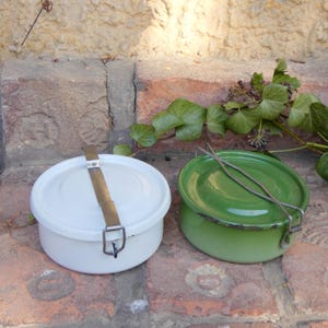Op de afbeelding: Twee vintage emaille lunchboxen, een witte en een groene, met metalen sluitingen en handvatten.