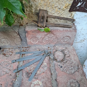 Może przedstawiać: Kolekcja zabytkowych narzędzi do obróbki drewna, w tym drewniany przymiar stolarski i metalowy zacisk sprężynowy. Narzędzia ułożone są na zwietrzałej ceglanej powierzchni, z zielonymi liśćmi w tle.