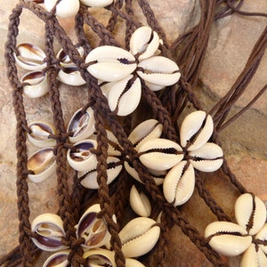 Peut inclure: Un bracelet fait main en cordon marron et coquillages de cauris. Les coquillages sont disposés en forme de fleur et sont liés ensemble par le cordon.