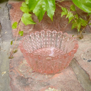 Könnte beinhalten: Eine rosa Glasschüssel mit Diamantmuster und einem gewellten Rand. Die Schüssel steht auf einer Steinoberfläche.