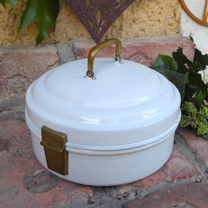Può includere: Contenitore di stoccaggio in smalto bianco con una maniglia e un chiavistello in ottone. Il contenitore ha una forma rotonda e una finitura bianca liscia.