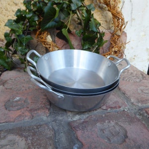 Puede incluir: Tres sartenes de aluminio plateado apiladas una encima de la otra. Las sartenes tienen un acabado metálico brillante y son ligeramente curvadas en los bordes.