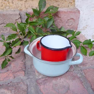 Può includere: Una pentola di smalto blu chiaro con un misurino di smalto rosso all'interno. Entrambi i pezzi hanno bordi neri.