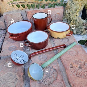 Può includere: Un set di sei articoli da cucina in smalto vintage, tra cui una tazza marrone, una ciotola marrone, una ciotola gialla, una pentola marrone, un colino marrone e un mestolo verde.
