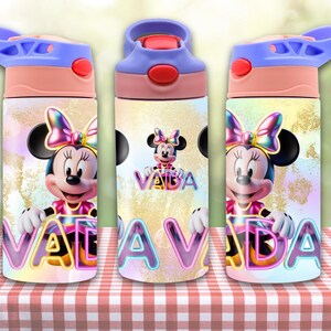 May include: Three water bottles featuring a Minnie Mouse design. Each bottle has a light blue lid, a pink top, and a colorful Minnie Mouse graphic with the name "VALADA". The bottles are on a red and white checkered surface.
